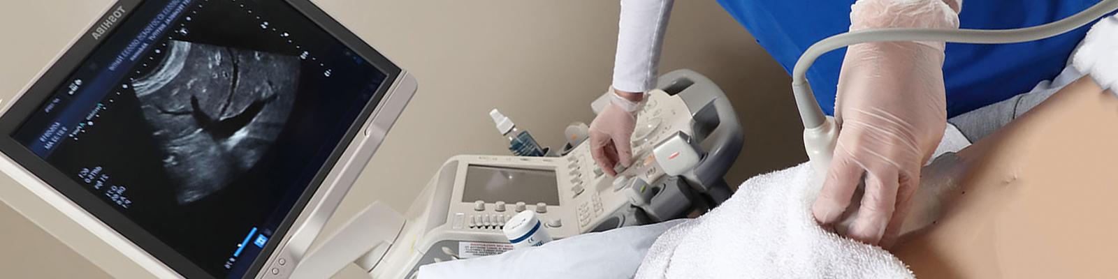 Student performing abdominal exam on patient with sonography machine, looking at screen